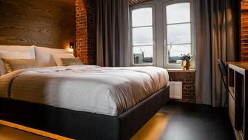 A modern bedroom with a large bed, a brick accent wall, a window with curtains, and a view of the city.
