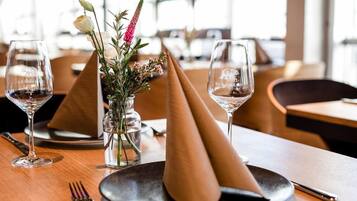 A dining table with two wine glasses, a vase with flowers, and a napkin cone.