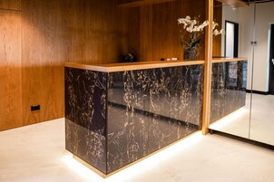 Una recepción con encimera de mármol, paneles de madera en las paredes y un florero con flores blancas.