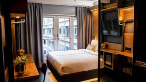 Una habitación de hotel con cama, escritorio, televisión y balcón con cortinas.