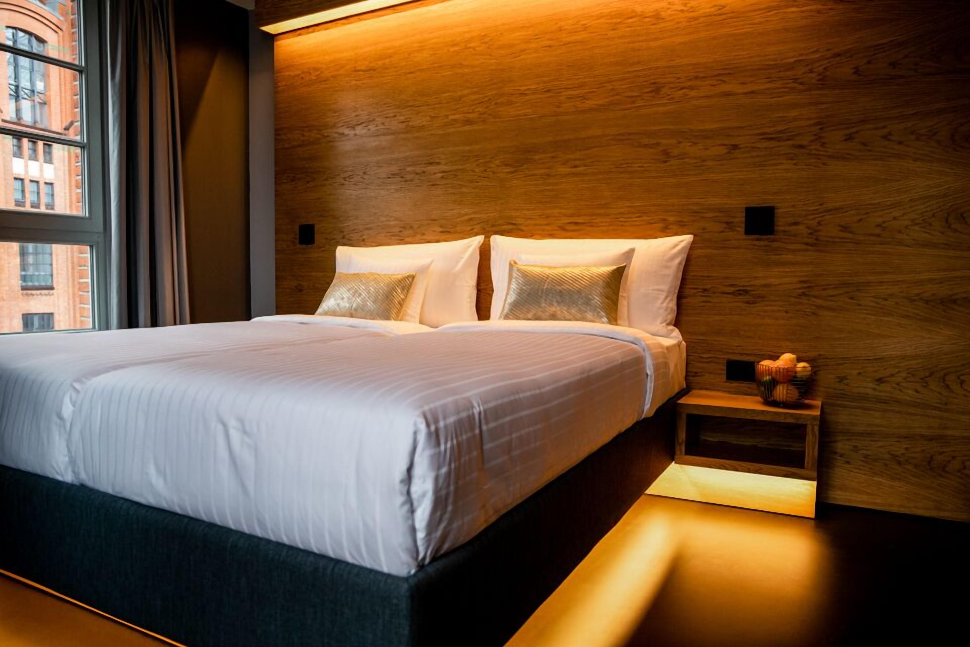 Quarto de hotel moderno com uma cama grande, cabeceira de madeira e mesa de cabeceira com abajur.