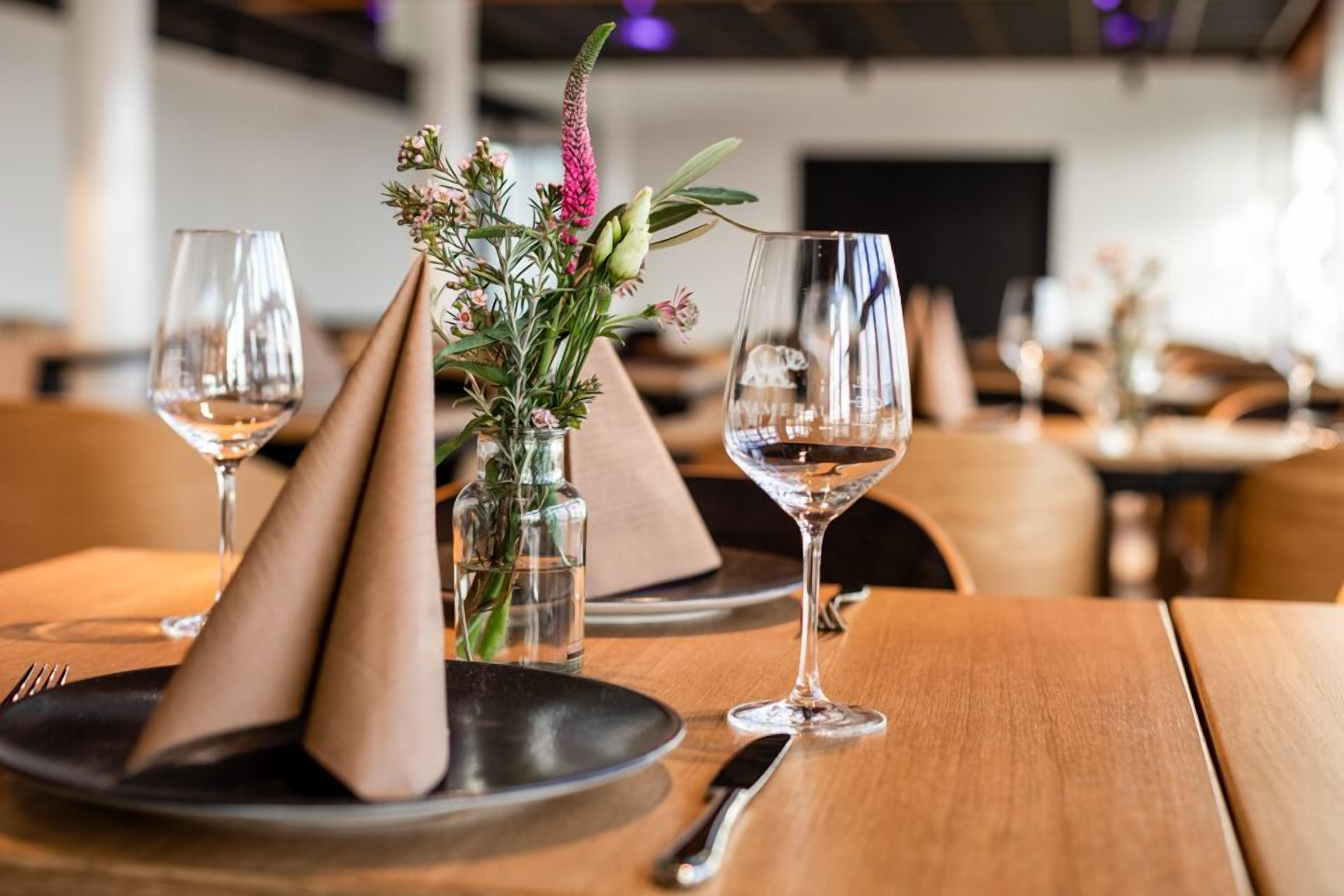 Uma mesa de jantar com um vaso de flores, dois copos de vinho e uma faca e garfo sobre uma mesa de madeira.
