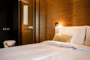 Ein Hotelzimmer mit Holz-Kopfteil, einem Bett mit weißer Bettwäsche, einem Nachttisch und einer wandmontierten Leuchte.