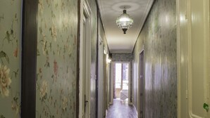 A hallway with floral wallpaper, wooden flooring, and a chandelier. - Pensión Amaiur (San Sebastián)