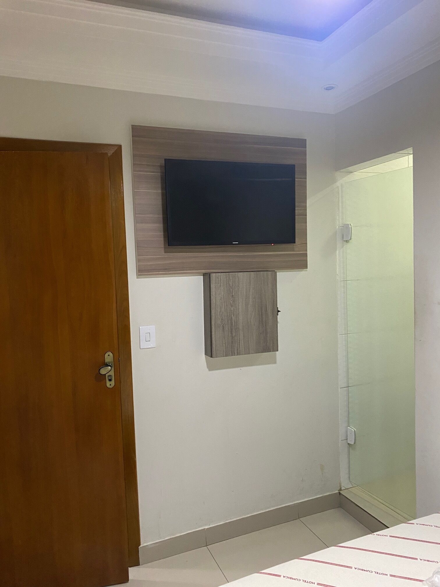 A room with a wooden door, a mounted flat-screen TV, a small cabinet, and a sliding door.