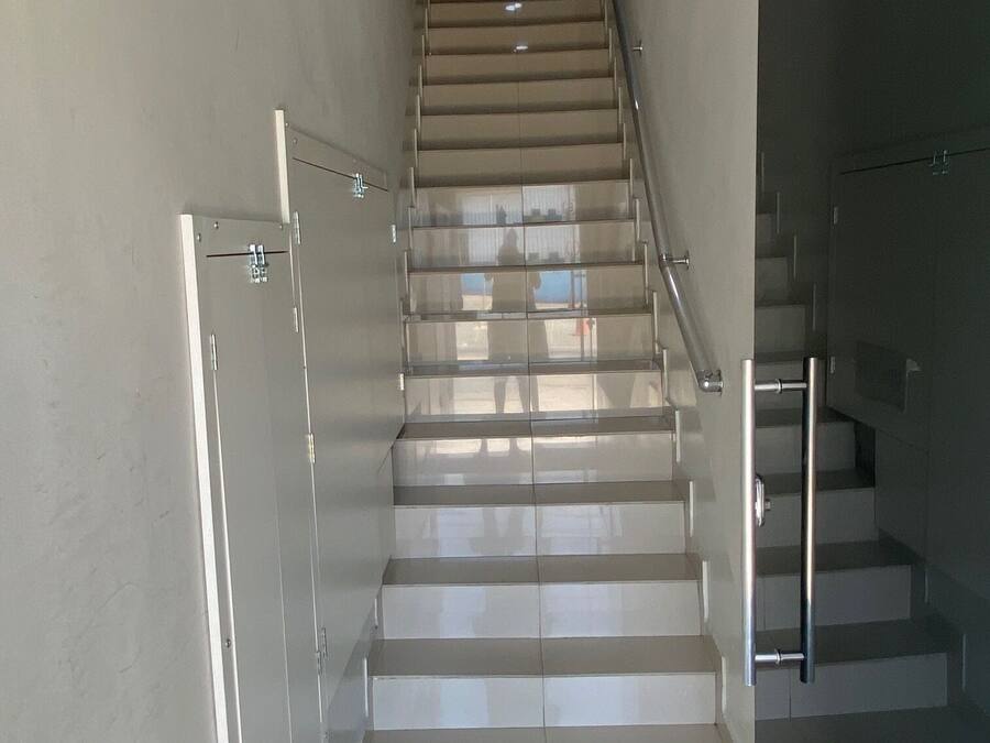 Uma escadaria moderna com guarda-corpos de vidro e corrimão de metal, que dá acesso a um andar superior.