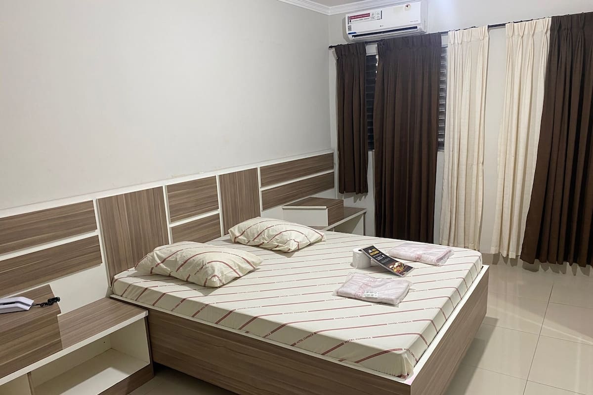 Une chambre d’hôtel comprenant un lit, des tables de chevet, une commode, un bureau et une fenêtre avec des rideaux.