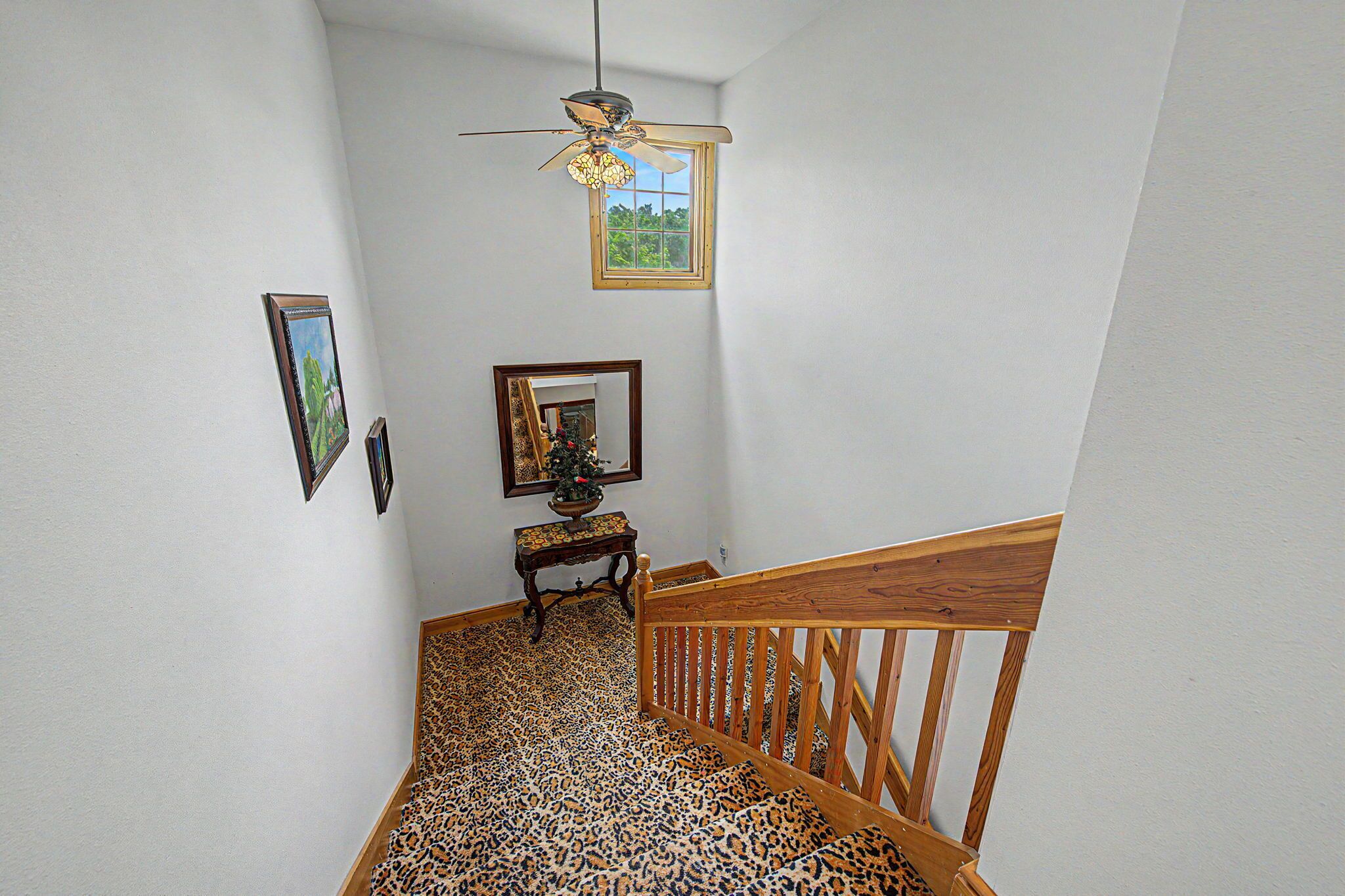 Una escalera con barandilla de madera, un ventilador de techo y una pequeña mesa con un árbol de Navidad.