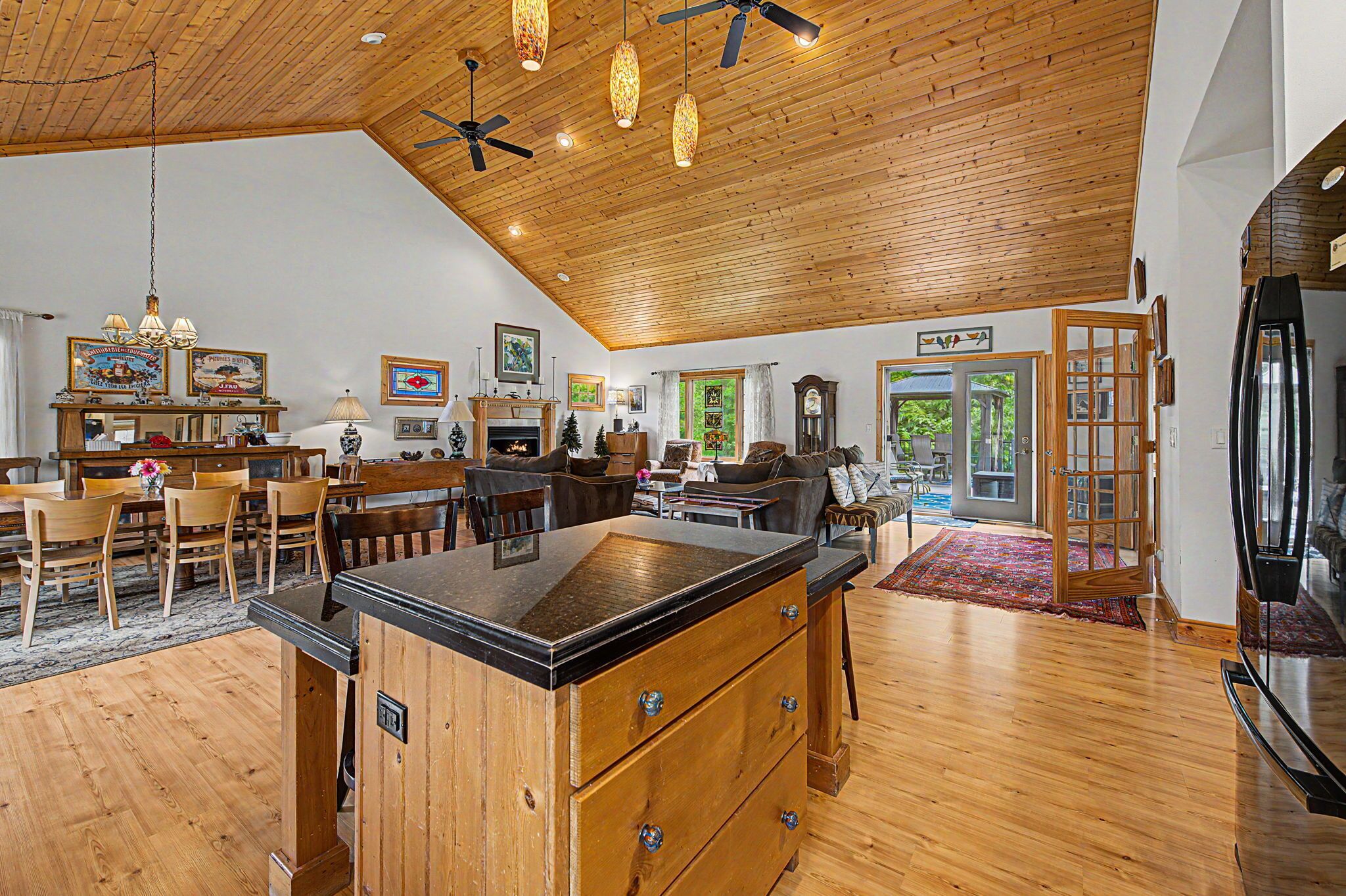 A spacious living area with a wooden ceiling, a dining table, chairs, a sofa, and a fireplace.
