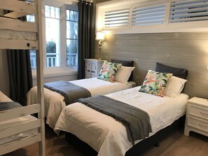 Ein Schlafzimmer mit zwei Betten, einem Nachttisch, einer Kommode und einem Fenster mit Vorhängen.