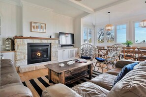 A living room with a stone fireplace, a television, wicker chairs, and a large window with a view.