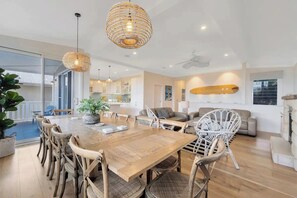 A spacious living area with a wooden dining table, wicker chairs, and a large window offering a view of the outside.