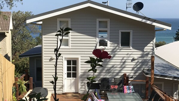A two-story house with a white exterior, a satellite dish, and a view of the ocean.