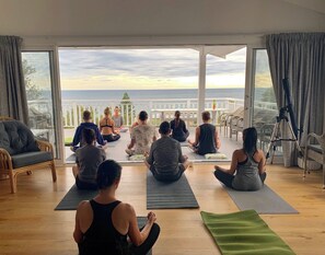 A group of people sitting on yoga mats in a room with large windows overlooking a scenic view.