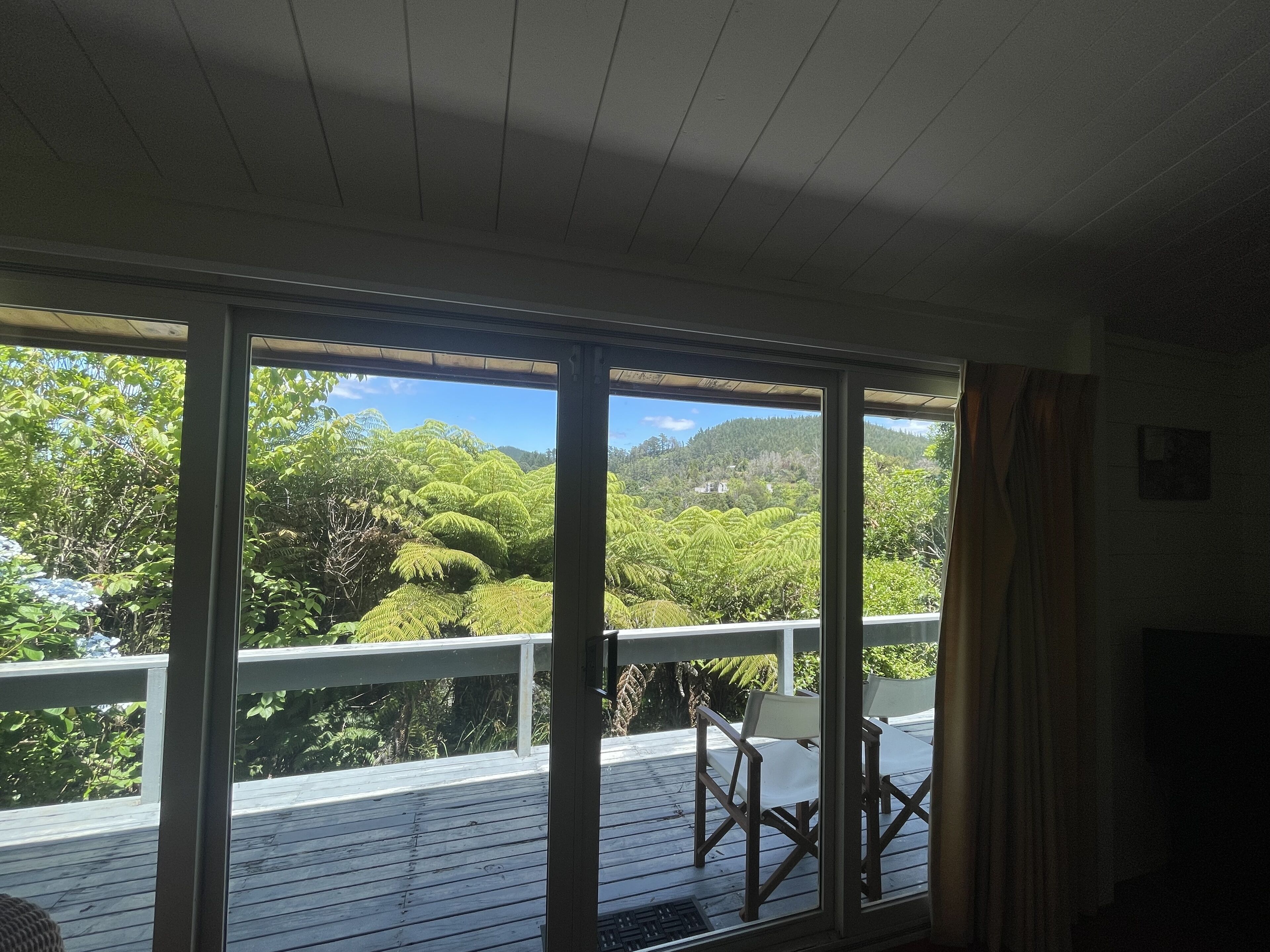 A room with large windows, a wooden deck, and a view of lush greenery and hills.