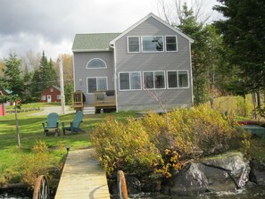 A two-story house with a deck, a small porch, and a dock leading to a rocky area. - New Beam construction house on pristine Back Lake (Pittsburg)