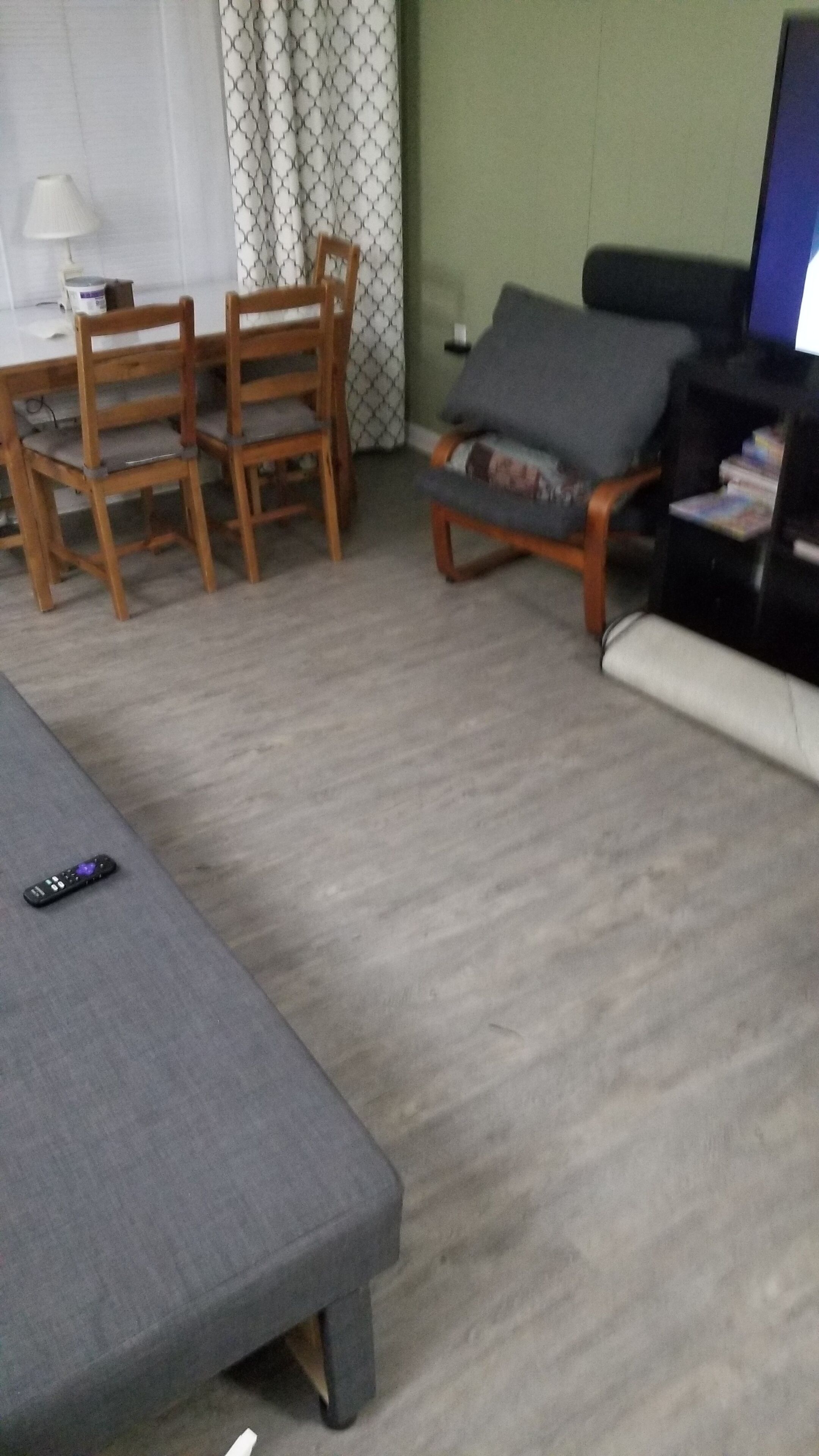 Ein Wohnzimmer mit grauem Sofa, Holzstühlen, einem kleinen Tisch und einem Fernsehschrank.