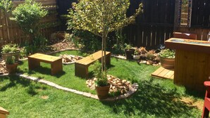 A backyard with a wooden fence, a small tree, and several wooden benches.