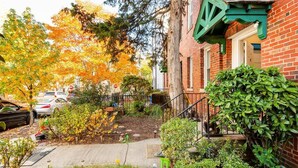 A residential area with brick houses, a garden with autumn foliage, and parked cars.