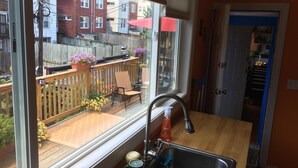 A kitchen with a window overlooking a backyard with a wooden deck, a chair, and potted plants.