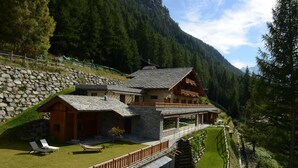 A chalet with a stone facade, wooden balconies, and a view of a forested mountain. - La Madonnina del Gran Paradiso (Cogne)