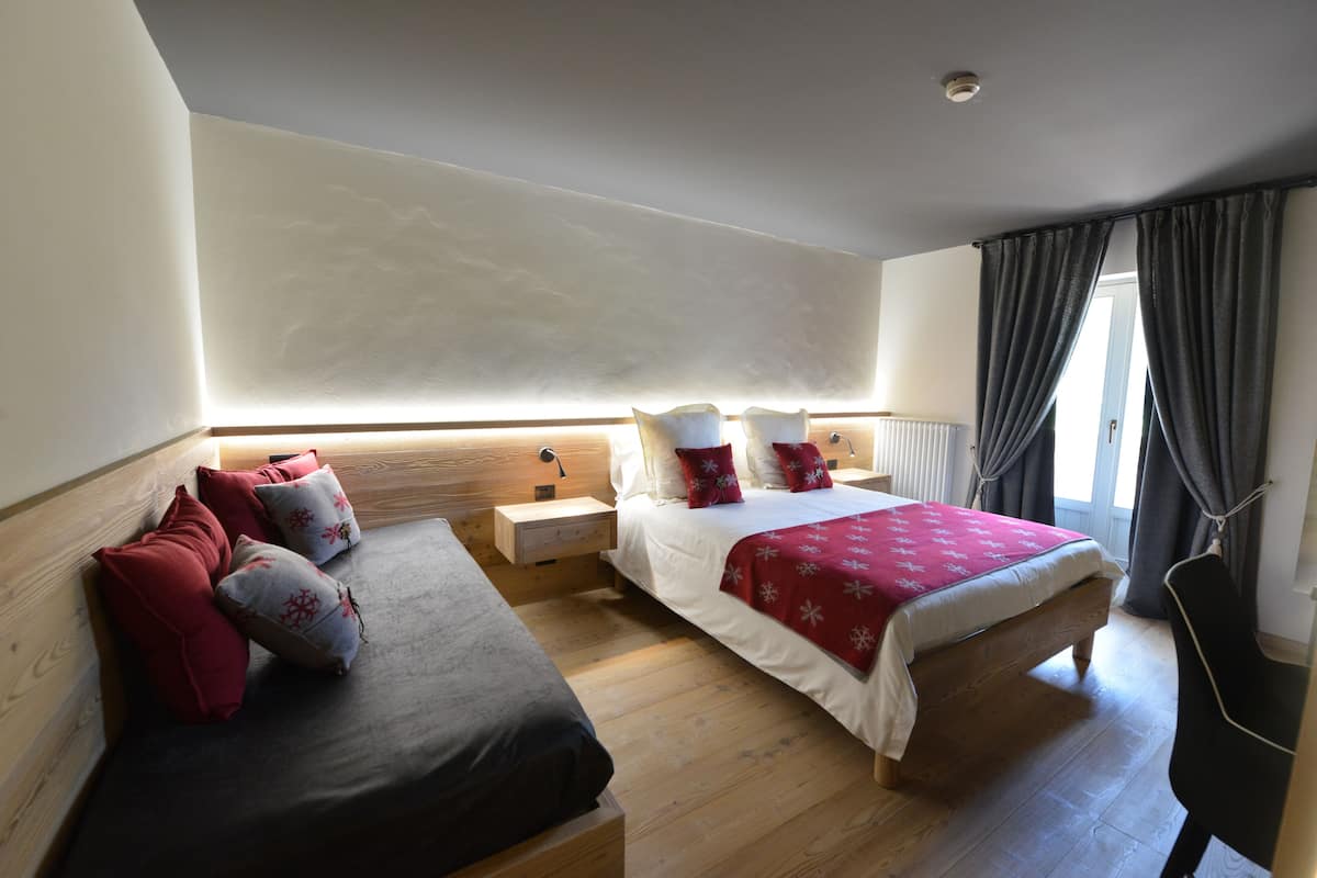 Une chambre avec deux lits, un plancher en bois, une table de chevet et une commode, ainsi qu’une fenêtre avec des rideaux.