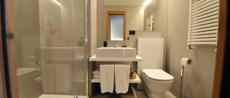 Un baño moderno con cabina de ducha de vidrio, un lavamanos blanco, un inodoro y una bañera.