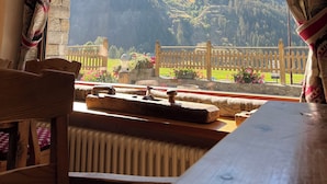 A room with a wooden table and chairs, a window with curtains, and a view of a mountain landscape. - La Madonnina del Gran Paradiso (Cogne)