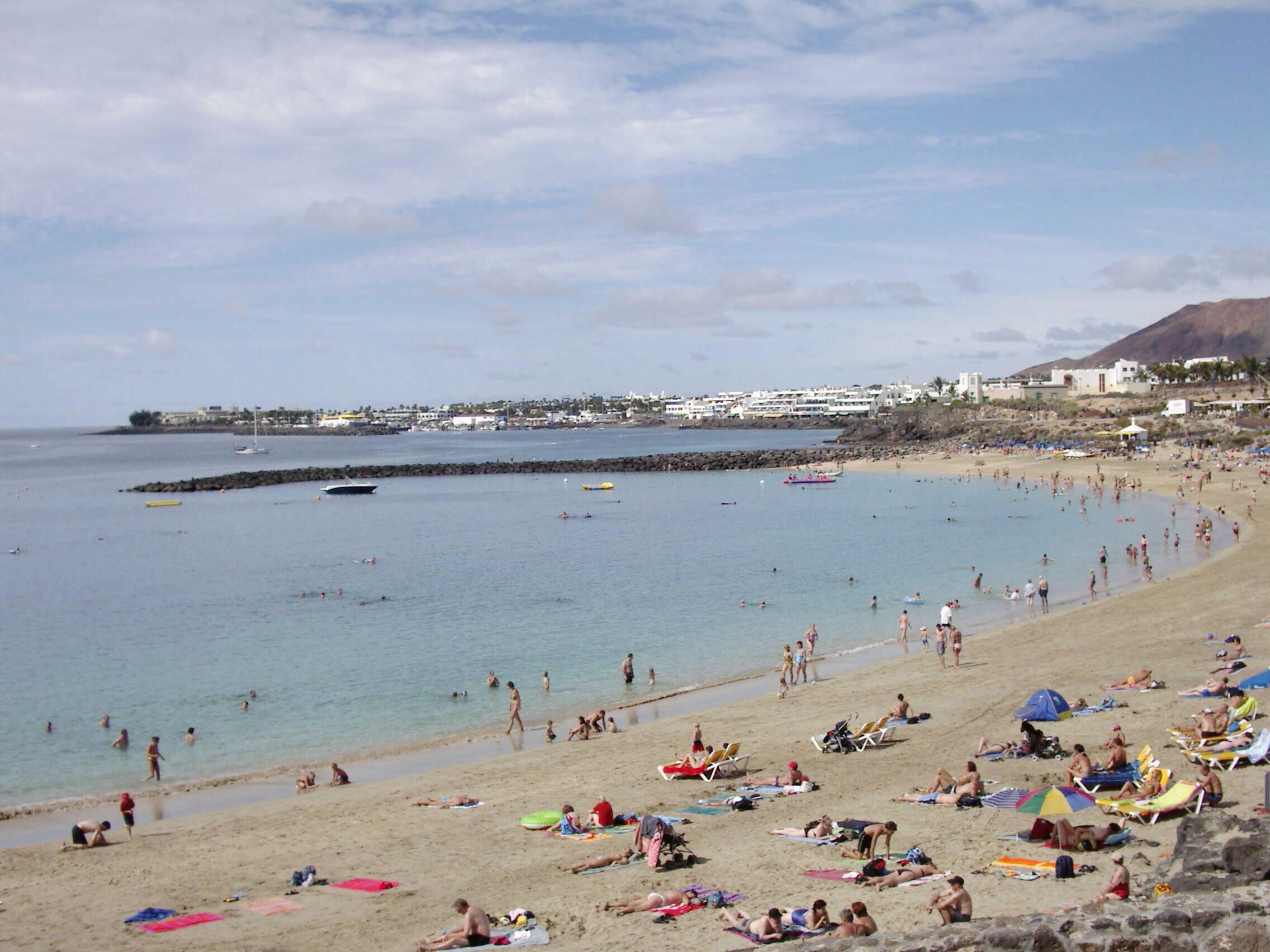 Una playa concurrida, gente tomando el sol y nadando.