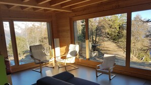 Ein modernes Ferienhaus-Interieur mit großen Fenstern, einer Couch und zwei Sesseln.