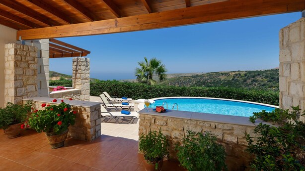 Zona de piscina con pared de piedra, sillas de descanso y vista al mar.