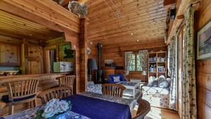 Interior acogedor de una cabaña con comedor, sala de estar con chimenea y una estantería.