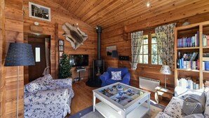 Interior acogedor de una cabaña de madera con chimenea, televisor, estantería y un espacio de estar confortable.