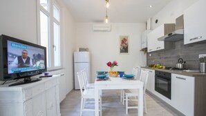 A modern kitchen with white cabinetry, a dining table set with blue plates, and a television displaying a program.