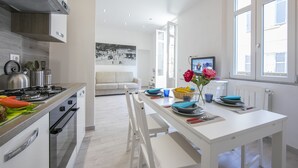 A modern kitchen with a dining area, white cabinetry, and a large window.