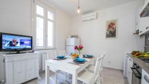 A modern kitchen with white cabinetry, a dining table with blue plates, and a television displaying a news program.