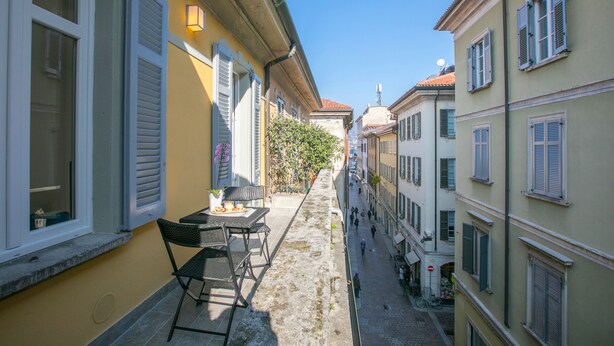 A narrow street with buildings on either side, a small outdoor seating area with a table and chairs, and a clear blue sky.