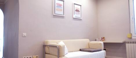 A modern living room with a beige sofa, a white rug, and two framed artworks on the wall.