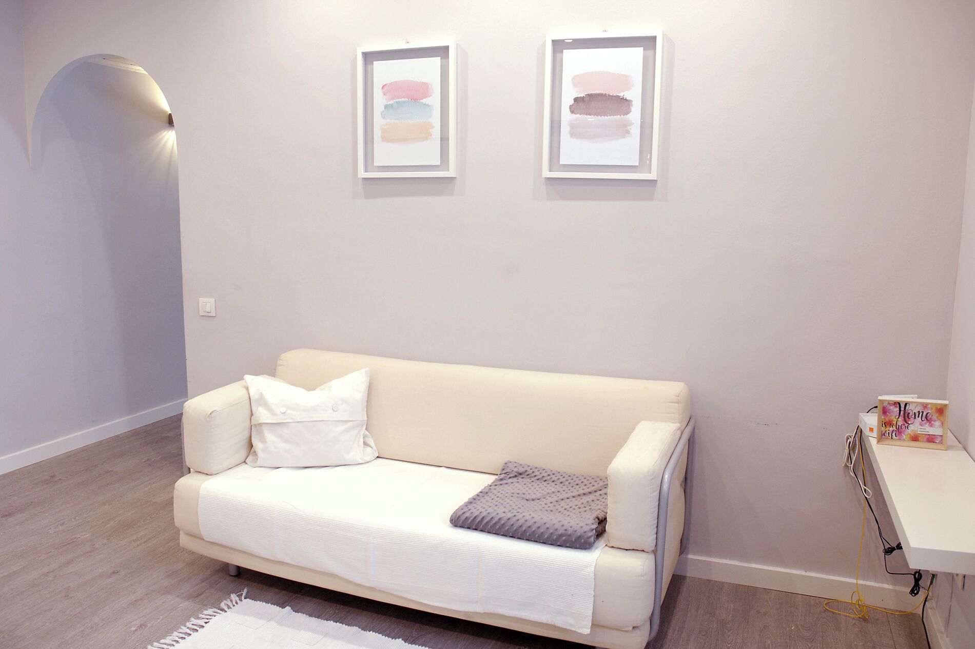 Una sala de estar moderna con un sofá blanco, una manta gris y dos cuadros abstractos en la pared.
