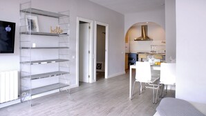 Un salon moderne avec un canapé blanc, un coin repas avec une table et des chaises, et une cuisine équipée d’une cuisinière et de placards.