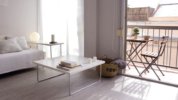 Une chambre à coucher moderne et bien éclairée, avec un lit, une table de chevet et un petit balcon équipé d’une table et de chaises.
