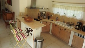 A compact kitchen with a central island, a built-in stove, and a sink. There is a trash bin and a window with curtains. - Upscale villa near UZES, private swimming pool, enclosed grounds, Wifi. (Collias)