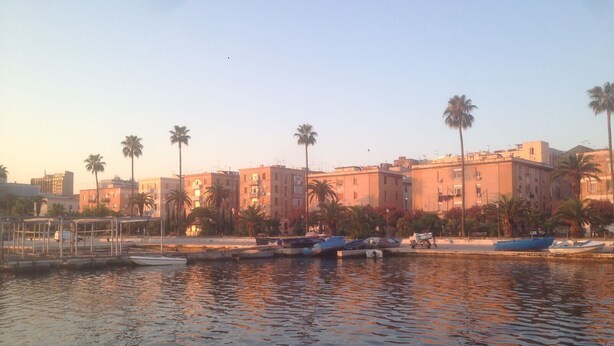 A waterfront area with buildings, palm trees, and boats docked along the shore. - Brau&Frau <br>apartment in Taranto (Taranto)