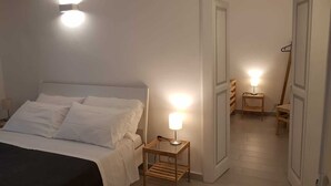 A bedroom with a bed, bedside tables, and a nightstand. There is a door leading to another room. - Brau&Frau <br>apartment in Taranto (Taranto)