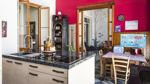 Una cocina con encimera de granito negro, armarios de madera, una pared de acento roja, una zona de comedor con mantel a cuadros y un mapa en la pared.