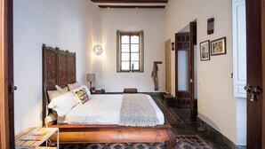 Un dormitorio con una cama de madera, una mesita de noche, un reloj de pared, una ventana y un suelo estampado.