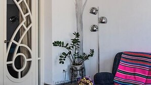 Una habitación con un mural de un árbol, una puerta blanca con patrones geométricos, una planta en maceta y una manta a rayas en una silla.