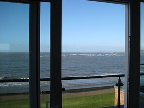A view from a balcony overlooking the ocean with waves crashing onto the shore. - 5* Self Catering Penthouse, Llanelli, Beach, Sea Views, Walks, Golf, Cycle. (Llanelli)