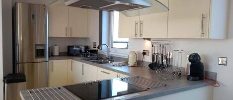 A modern kitchen with a stainless steel refrigerator, a built-in microwave, a kettle, and a coffee maker.