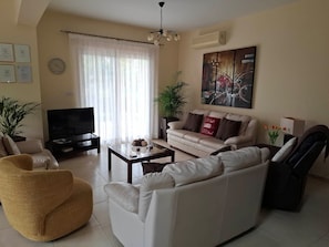A living room with a sofa, armchair, TV, coffee table, and a large window with curtains.
